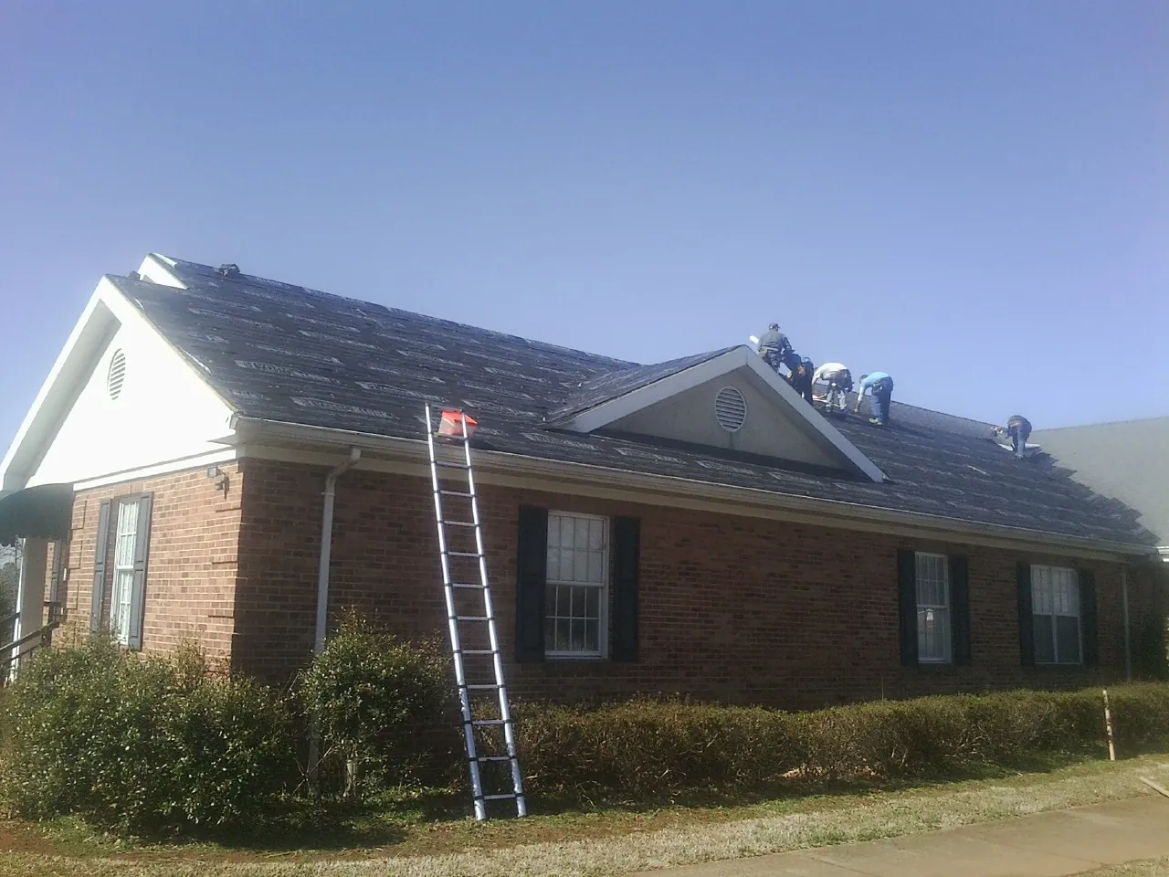 Crew tearing shingles off a brick ranch roof with a ladder set — Emergency Roof Repair work by our crew in Arthur