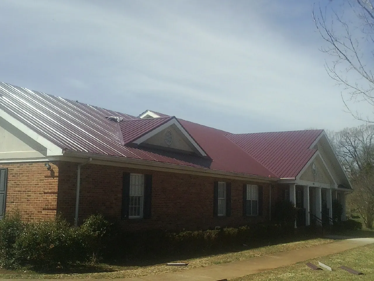 Red metal roof with gabled entries on a long brick building, from a Hail Damage Roof Repair job in Arthur