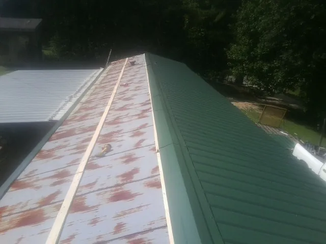 Old rusted panels beside newly installed green metal roofing — Wind Damage Roof Repair by Roofing Brothers in Arthur