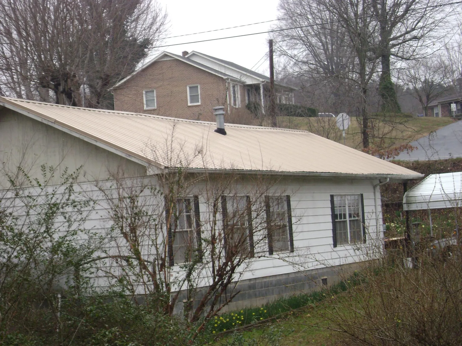 Tan metal roof on a white sided house set into a hillside — Commercial Roofing by Roofing Brothers in Arthur