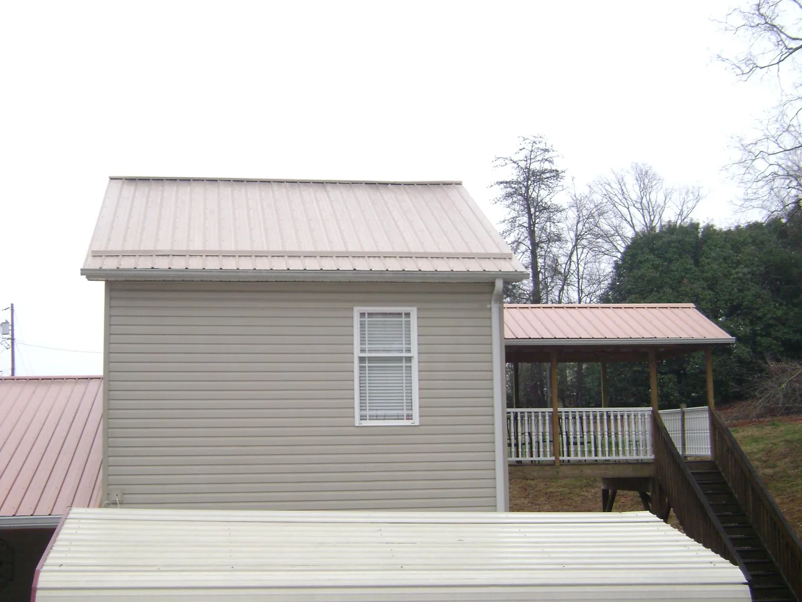 Tan metal roofs on a two story addition and attached porch, from a Roof Replacement job in Arthur